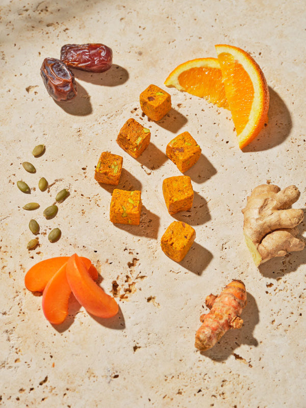 GEM bits on a counter surrounded by ingredients like ginger, orange, turmeric, pumpkin seeds, and dates