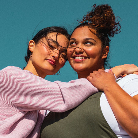 woman in pink sweater and woman in green overalls hug